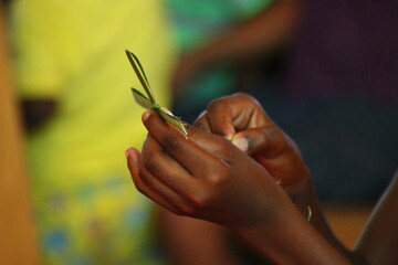 Child in Africa folding palm leaves to a spritual cross during a religious sermon

