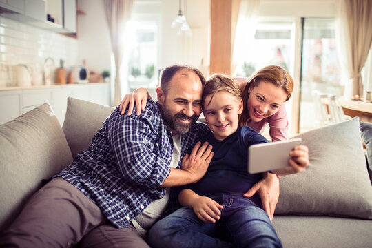 Happy young family taking selfie at home on couch
