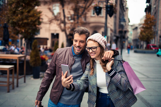 Happy young couple using smartphone while shopping in city