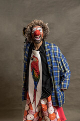 A cheerful curly-haired clown grimaces. Portrait against a background of beige wings. The clown in the parrot tie