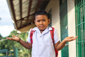 A young southeast asian school boy shrugs, not knowing the answer while being questioned. Outside a...