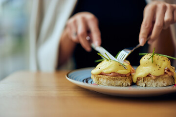 Close-up of a female hands, cutting an egg toast in half, using a fork and a knife.