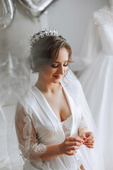 A beautiful brunette bride with a tiara in her hair is getting ready for the wedding in a beautiful robe in boudoir style. Close-up wedding portrait, photo.