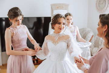 Morning of the bride. The bride's maid of honor helps the bride lace up her dress, fasten buttons...