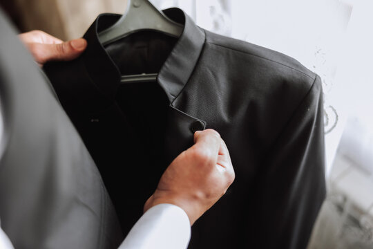 the man holds his black jacket on a hanger in his hands. The groom is preparing for the wedding ceremony. Detailed close-up photo of hands