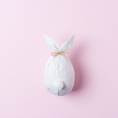 Easter egg wrapped in a paper in the shape of a bunny. Minimal Easter concept.