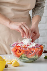 Obraz na płótnie Canvas Woman adding feta cheese to bowl of Greek salad