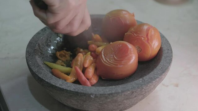Close-up shots on process of making Indonesian traditional chili sauce named "sambal terasi or sambal ulek" crushed on mortar from Top View and seasoning with spices