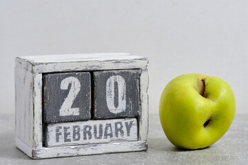 February 20th on wooden calendar and green apple on white background. Apple Day USA.