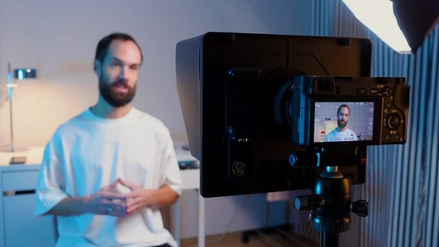 A young male blogger records a video with teleprompter for his YouTube channel in his studio.