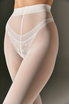 cropped view of woman in white lace panties and pantyhose posing on grey background, close up