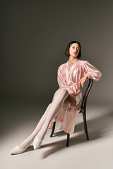 alluring young asian woman in pink silk robe and white tights sitting on chair on grey background