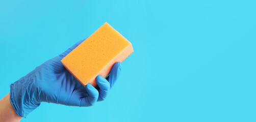 Cleaning the room, sponge in hand close-up. Female hand in a blue latex glove with a sponge for washing dishes or wet cleaning, blue background. Cleaning service