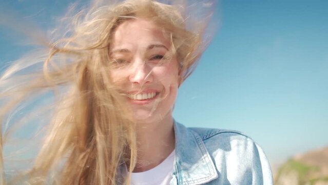 Closeup of young woman face covered with flying hair in windy day. Portrait female with hair blowing in the wind. Wanderlust autumn travel, atmospheric moment. Slow motion