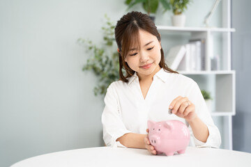 貯蓄を象徴するピンクの貯金箱にコインを入れる女性