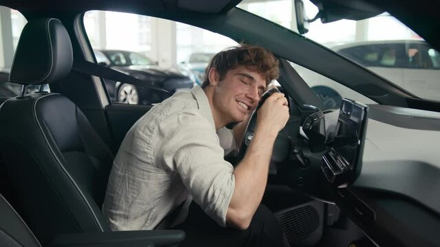 Caucasian client man buyer guy customer male sitting in luxury new car choosing auto visit showroom choose automobile rent test drive buying enjoy vehicle choice embrace hug cuddling wheel steering