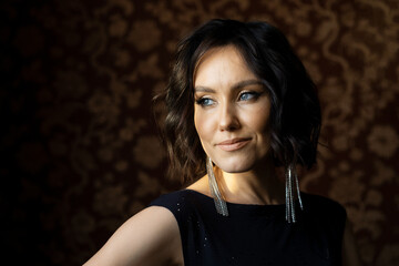 Portrait of a young beautiful brunette with gray eyes in long earrings with a smile on her face