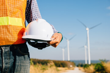 Engineer stands at wind turbine field holding safety helmet. A symbol of renewable success...