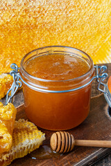 A glass jar of thick golden honey with wooden spoon and honeycombs. Concept of beekeeping,...
