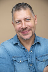 Obraz premium cool man, 46 age, with grey hair, blue jeans, blue shirt, posing in front of brown studio, portrait, concept, business, casual