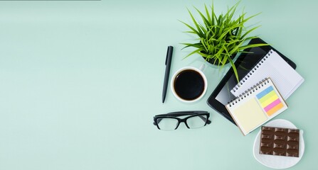 Office desk, top view, with tablet, pen and notepad, glasses, cup of coffee, green background. ...
