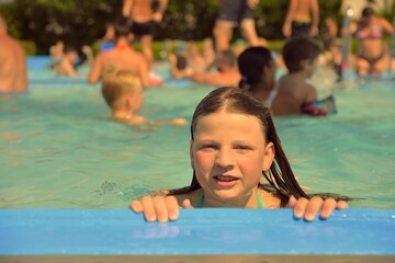 A little girl at the edge of the pool. Little girl in the pool. Young woman on the edge of the...