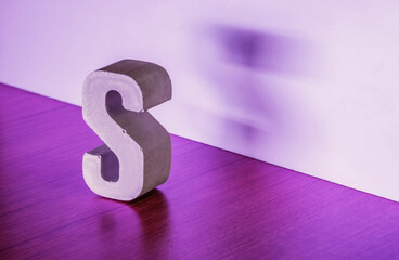 Letter S made of concrete material stands on wooden floor. Selective focus.