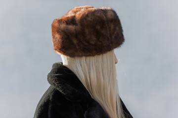 Slavic bimbo aesthetic. Portrait of a European type Blond head Young woman with natural skin in fur unisex hat.  