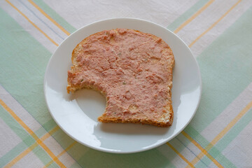 slice of bread with liver pate that has been eaten a bit off on a white plate on an old tablecloth