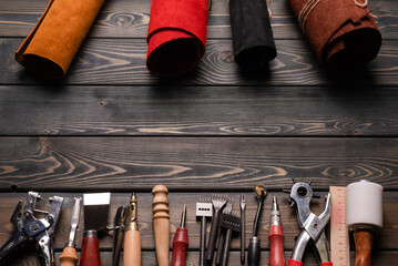 Leather pieces and leather craft work tools on the old wooden workbench background top view with...
