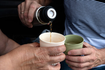 A man pours tea or coffee from a thermos into reusable bamboo glasses outdoors