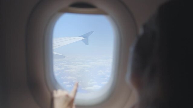 Woman flying in airplane and looking outside at wing over clouds in blue sky