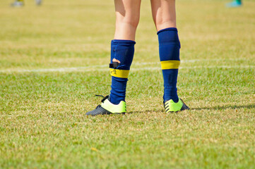 Detail of a young soccer player's legs, on a grassy field, wearing worn-out socks and cleats