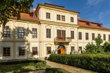Svojsin, Czech Republic - October 13 2023: Front view of the newly renovated castle, a yellow building with red roof and the park with green bushes and trees. Sunny autumn day with blue sky.