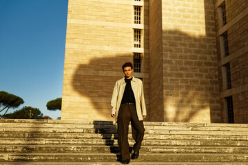 Handsome Italian Caucasian boy dressed well climbs the stairs for photo shooting. The man looks or...