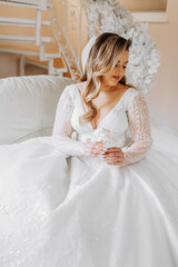 Beautiful bride in a luxurious wedding dress with a fashionable wedding hairstyle, professional make-up. Close-up portrait of young gorgeous bride in room from morning. High quality photo.