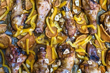 Chicken legs with sweet potato, yellow pepper and garlic after roasting in the oven. Top view.