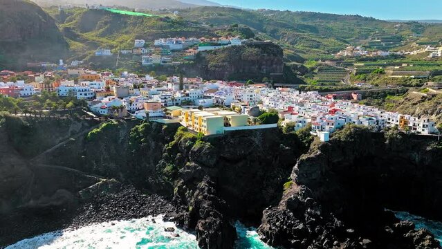 Aerial view of stone houses with red tiled roofs and delightful wooden balconies on the cliffs in Tenerife. View from above of colourful coastal La Laja natural pool in San Juan de la Rambla, Canary.