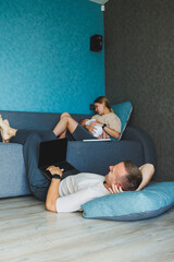 Parents with baby sitting on sofa at home with laptop and talking online. A young family with a child works on a laptop at home while sitting on the sofa.