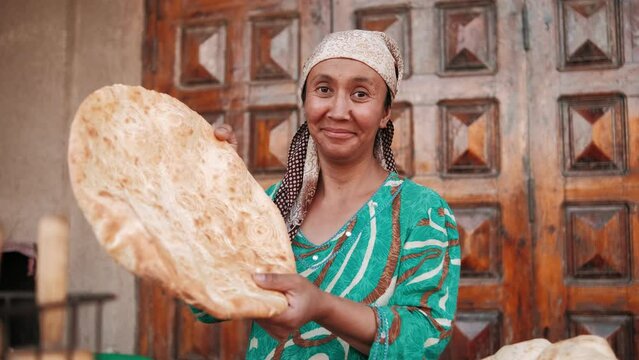 Eastern woman prepares flatbread using traditional method. East market. Elderly asian woman in colorful national clothes prepares bread. Uzbekistan, Khiva