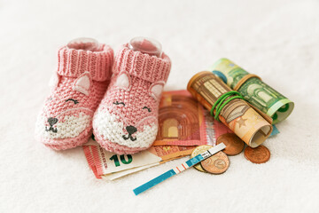 Pregnancy and motherhood concept. Children's knitted socks, pregnancy test and money on a white...