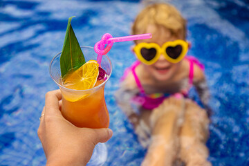 A woman in the pool drinks a cocktail. Selective focus.