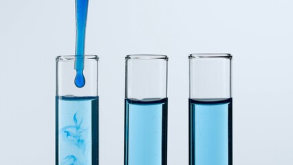Three glass test tubes on a white background. Test tubes are filled with blue liquid, a blue substance is dripping into one of them from a pipette. Concept of medicine, biochemical research. Close-up.