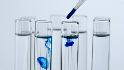 Close up laboratory glassware on white background. Test tubes with transparent liquid. Person adds...