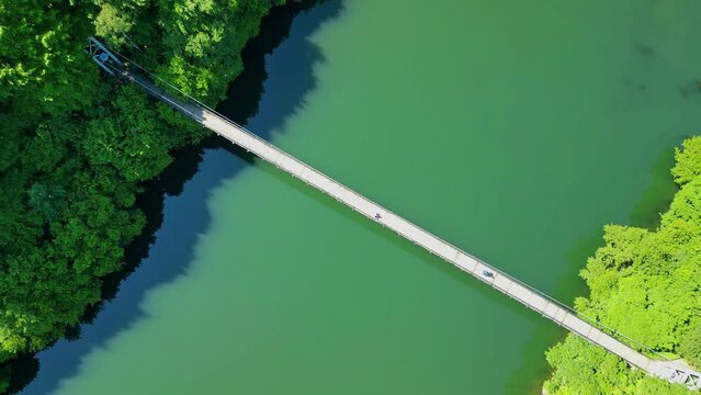 Drone view Rope Bridge over Pasarel dam, water reflection, autumn trees and a fisherman

