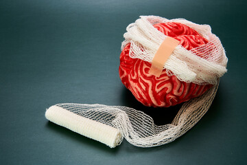 Representation of a bandaged red brain with a dark background, concept of brain damage.