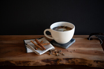 White tea mug with warm tea with apple slice and cinnamon sticks on wooden table with mulling spices