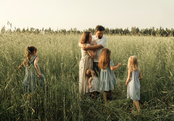 Family portrait on a field in rye in the rays of the setting sun. Father and mother hug their...