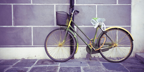 Old rusty women's bicycle against a plaster wall in a italian street paved of stone