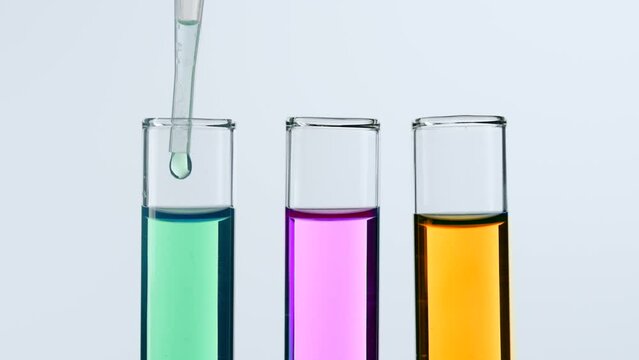 Concept of science and biotechnology. Closeup of laboratory utensils on white background. Test tubes filled with pink, green, yellow liquid, scientist pipetting green liquid from test tube. Slow